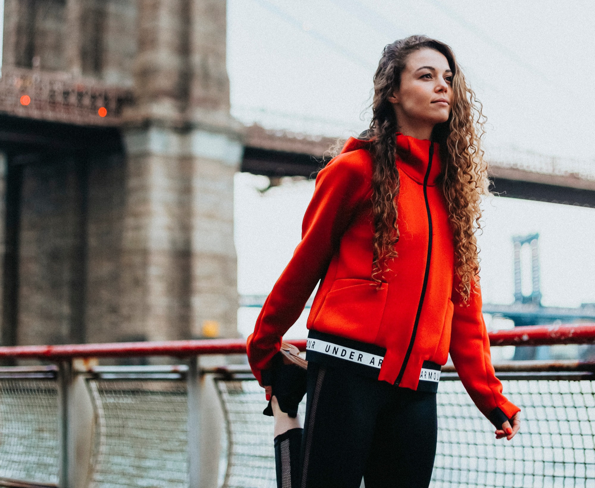 Lauren Mazzo in an orange jacket on a New York City bridge